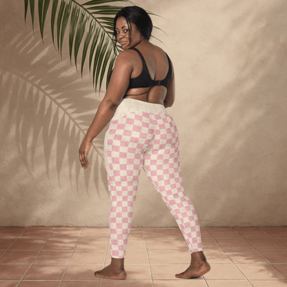 Woman wearing pink checkered leggings and black sports bra against a beige wall.