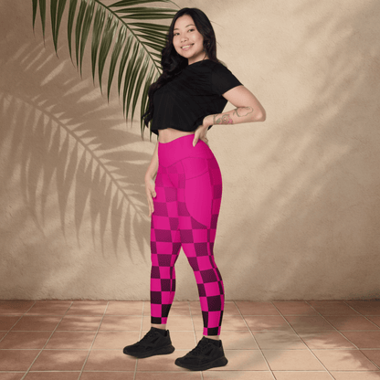 Woman wearing pink checkered leggings and black top standing against a beige wall with a plant.