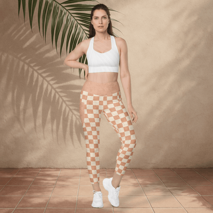 Woman wearing a white sports bra and checkered leggings standing against a beige wall with a plant.