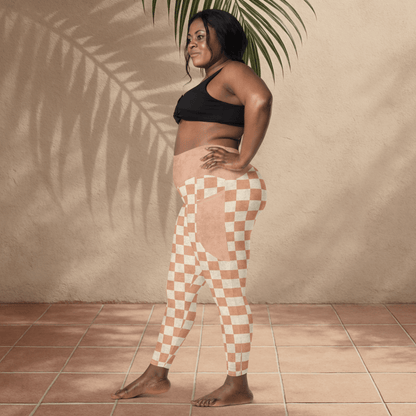 Woman wearing a black sports bra and checkered leggings standing against a beige wall with a plant.