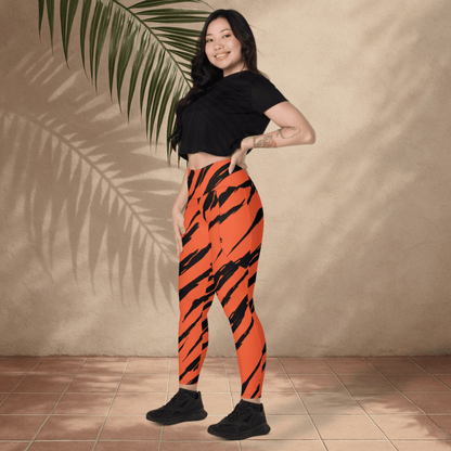 Woman wearing orange tiger stripe leggings and black top standing against a beige wall with a plant.