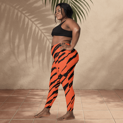 Person wearing black sports bra and orange tiger stripe leggings standing against a beige wall.