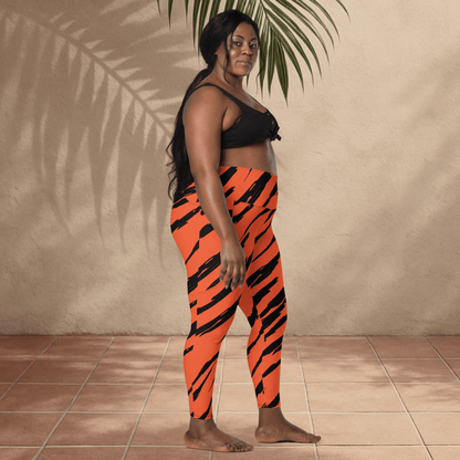 Woman wearing black sports bra and orange tiger stripe leggings standing against a beige wall.