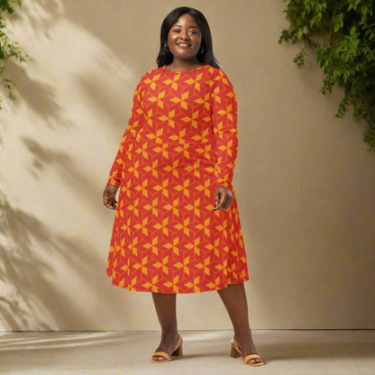 Woman wearing a red and yellow patterned dress standing against a beige wall with greenery.