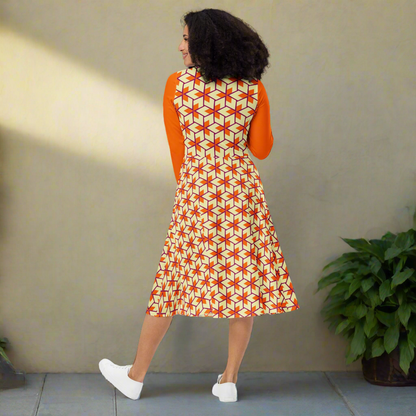 Curly-haired model facing away from the camera, revealing the back of a vibrant triangle-patterned midi dress with solid orange long sleeves. The flared skirt gently widens from a fitted waist, and the pattern continues seamlessly across the back. The soft gray background highlights the bold colors of the dress.