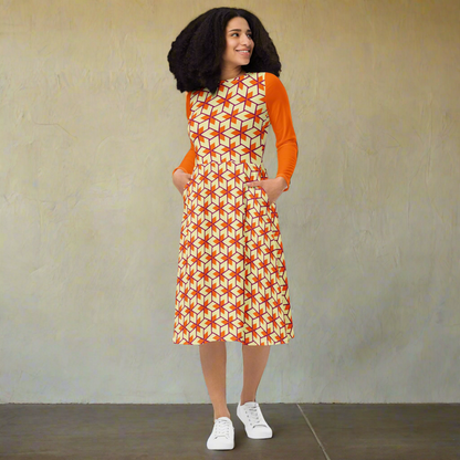 Curly-haired model walking toward the left with a light, joyful expression. Her dress flows with motion, showing the pattern and structure of the flared skirt, orange sleeves, and side pockets.