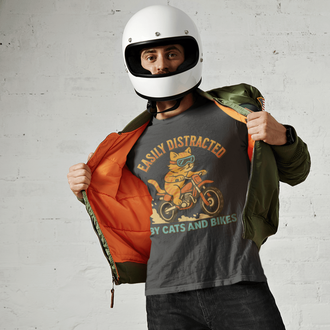 Person wearing a helmet and holding an orange lined jacket with a cat riding a dirt bike graphic design on a white brick wall background