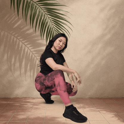 Woman in black t-shirt and pink patterned pants sitting on the floor with a plant leaf above her head.