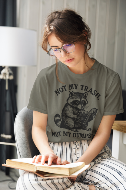 Woman wearing a green t-shirt with a raccoon graphic and text, sitting on a chair reading a book.