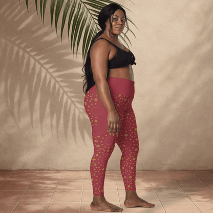 Woman wearing scarlet leggings with gold patterns and a black top, standing against a beige wall with a palm leaf.