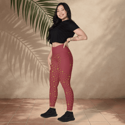 Woman wearing maroon leggings with gold patterns and a black top, standing against a beige wall with a palm leaf.