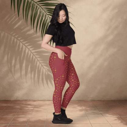 Woman wearing red patterned leggings and black top against a beige wall with a plant leaf.