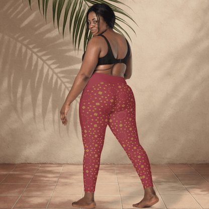 Woman wearing red patterned leggings and black sports bra against a beige wall.