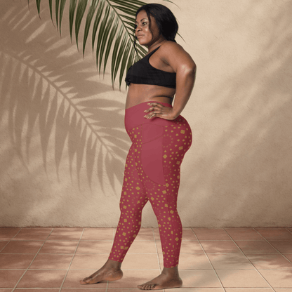 Woman wearing scarlet leggings with gold patterns and a black sports bra against a beige wall.