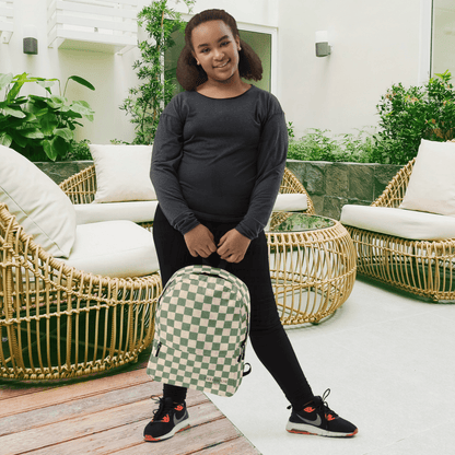 Person holding a green and white checkered backpack in an outdoor setting with wicker chairs and plants.