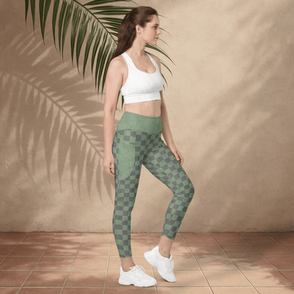 Woman wearing green checkered leggings and white sports bra against a beige wall with a palm leaf.