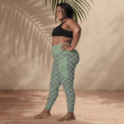 Woman wearing green checkered leggings and black sports bra standing against a beige wall.