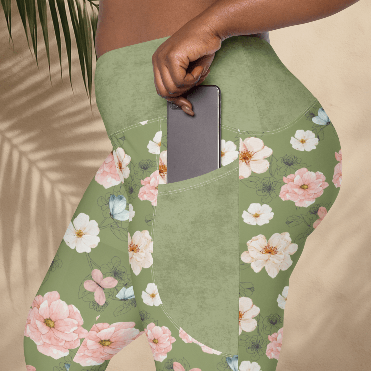 Green floral leggings with a pocket holding a phone, against a beige background.