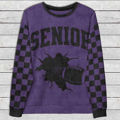 Purple sweatshirt with 'SENIOR' and football graphic on a wooden surface