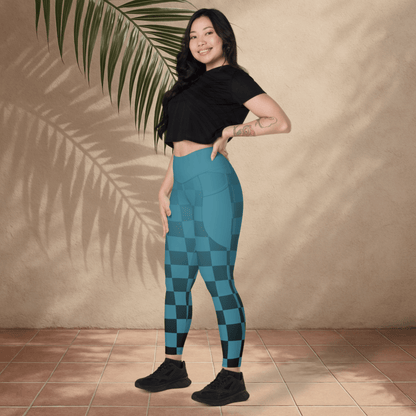 Woman wearing blue checkered leggings and black top standing against a beige wall with a plant.