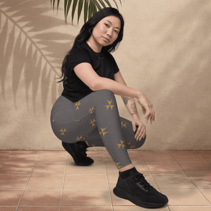 Woman wearing black t-shirt and gray leggings with yellow patterns, sitting on a tiled floor.