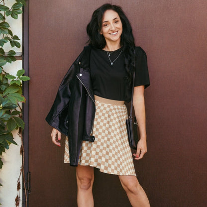 Woman wearing a black top and checkered skirt against a brown wall.