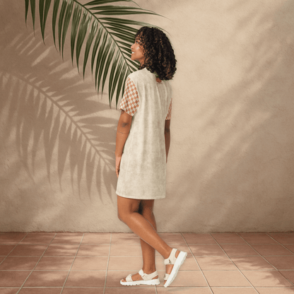 Woman in a light dress standing against a beige wall with a palm leaf