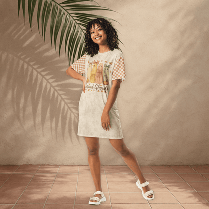 Woman wearing a ghost checkered t-shirt dress standing against a beige wall with a plant leaf.