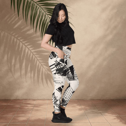 Woman wearing black and white patterned leggings against a beige wall with a palm leaf.