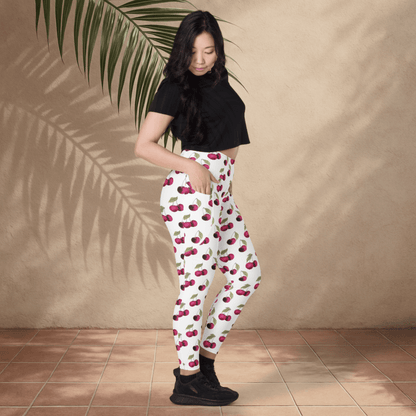 Woman wearing cherry-patterned pants against a beige wall with a plant.
