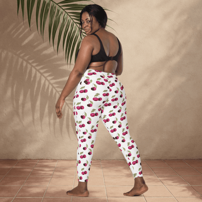 Woman wearing cherry-patterned pants standing against a beige wall with a plant.