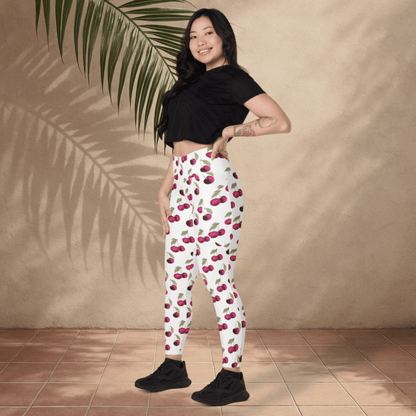Woman wearing cherry-patterned pants standing against a beige wall with a palm leaf.