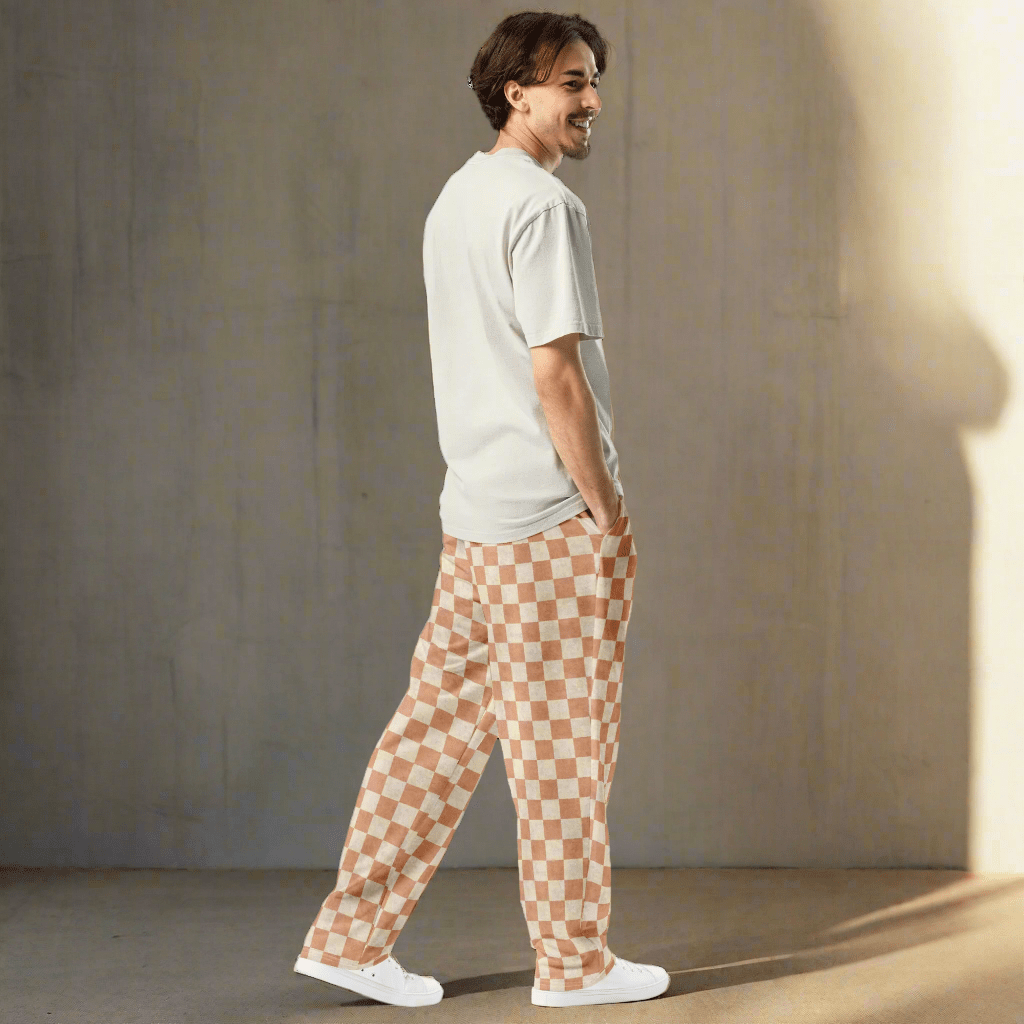Man wearing a white t-shirt and checkered pants against a neutral wall.