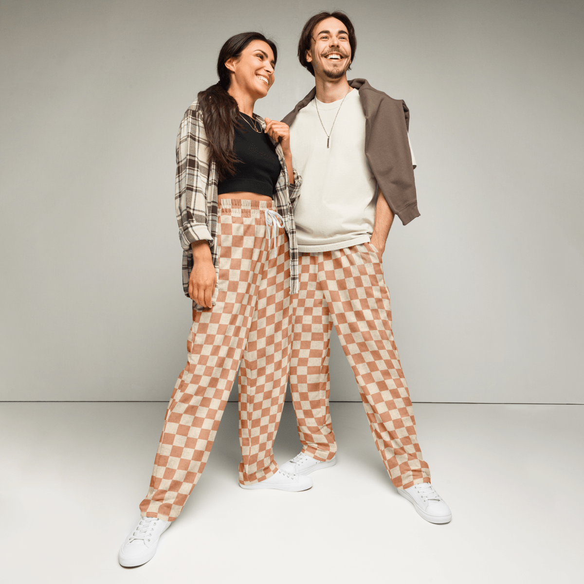 Two people wearing matching checkered pants against a plain background