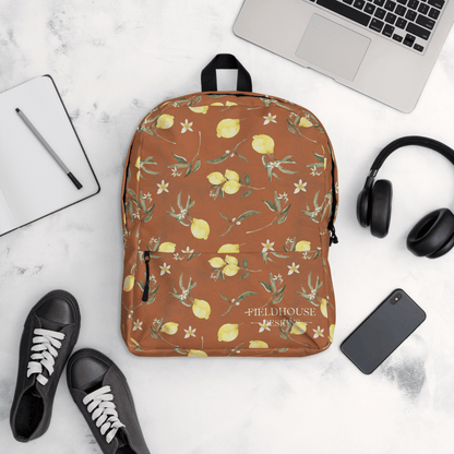 rust backpack with lemon pattern on a white surface with laptop, phone, and shoes.