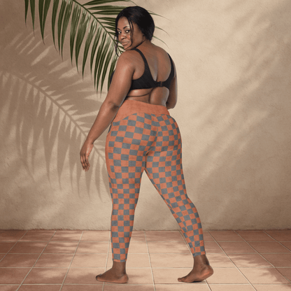 Woman wearing checkered leggings standing against a beige wall with a plant leaf.