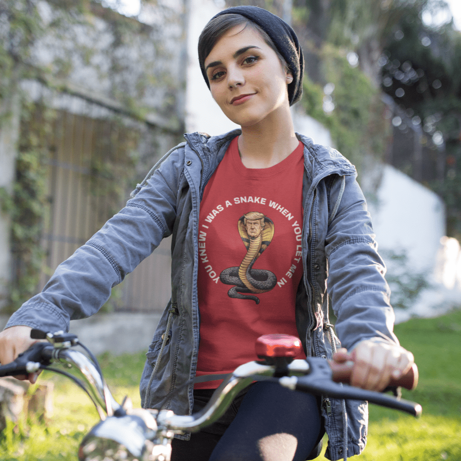 Person wearing a red t-shirt with a snake graphic and text, riding a bicycle outdoors.