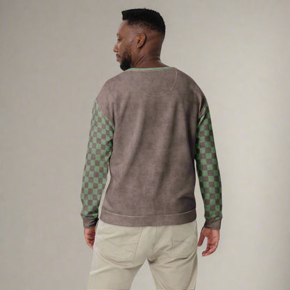 Man wearing a brown sweater with green checkered sleeves on a neutral background