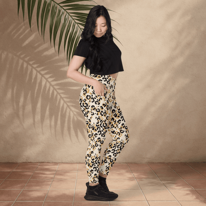 Woman wearing a black top and leopard print pants standing against a beige wall with a palm leaf.