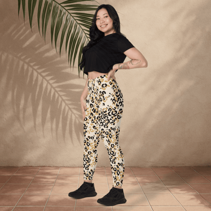 Woman wearing leopard print pants and a black top standing against a beige wall with a palm leaf.